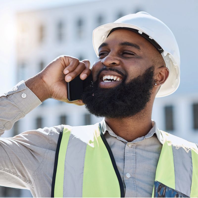 African engineer man, phone call and city with smile, thinking and listening for networking, building or development. Construction site manager, smartphone and ideas for property, helmet and safety