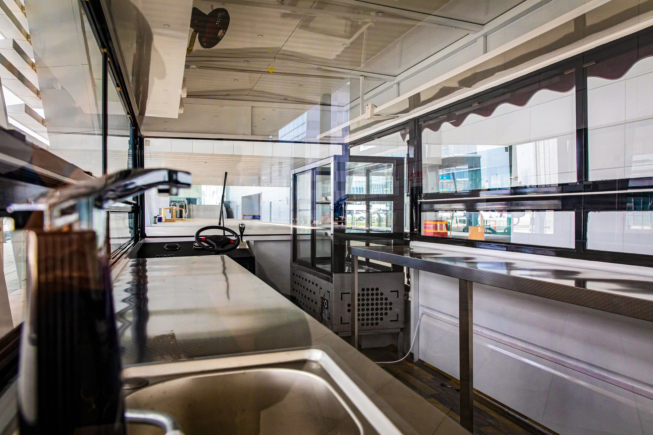 Interior of a modern food truck with stainless steel counters and a steering wheel.
