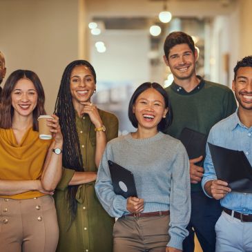 A diverse group of five smiling young professionals standing together indoors.