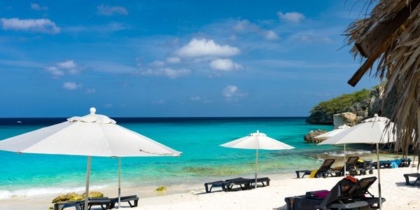 Sunny beach with white umbrellas and turquoise water under a clear blue sky.
