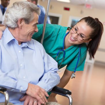 Nurse smiling and comforting elderly man in wheelchair at hospital.