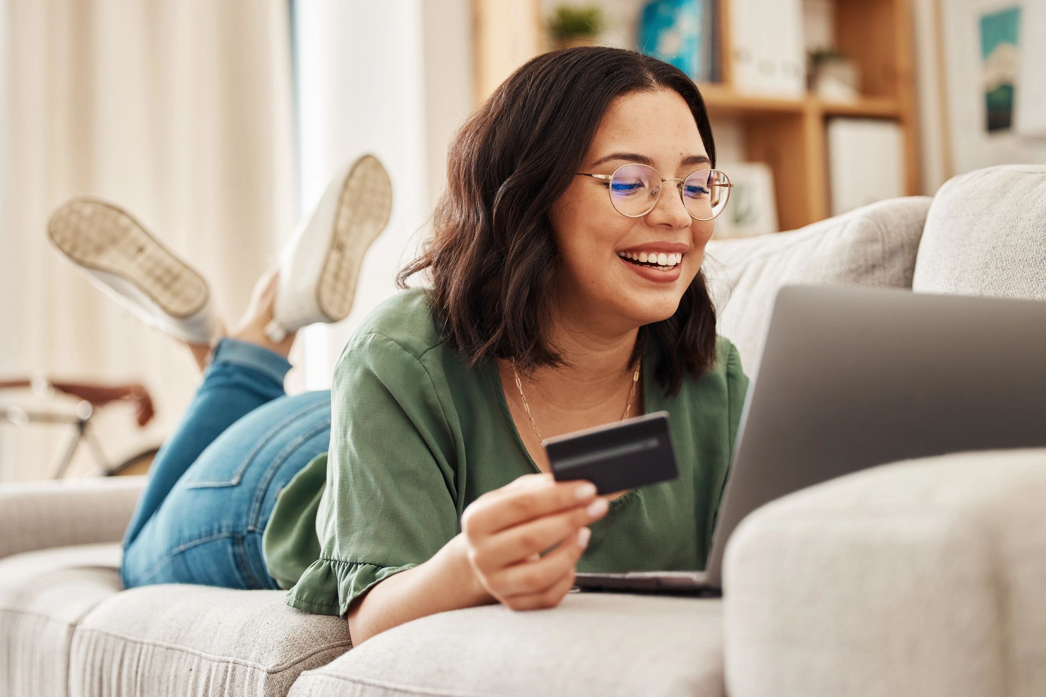 Lady laying on a couch with a credit card in hand in front of a computer