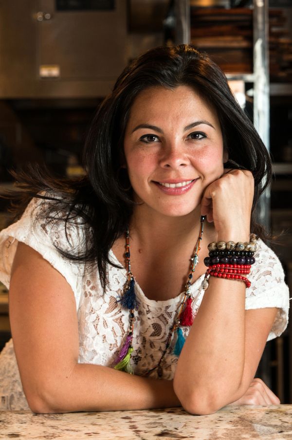 Smiling woman with colorful bracelets and necklaces, leaning on a marble table.