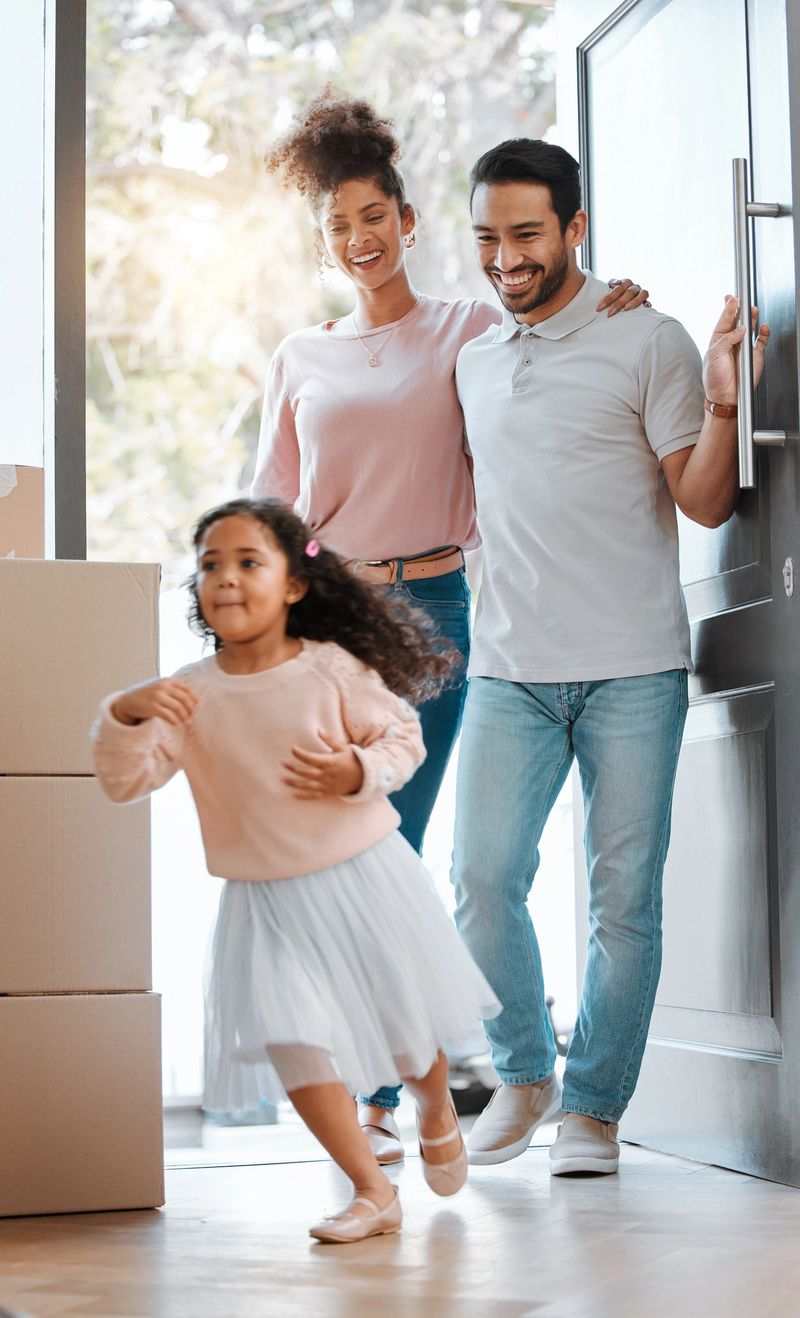 Happy family, real estate and moving in new home for investment, property or fun relocation by door. Father, mother and daughter smile playing in house for mortgage loan, renovation or beginning