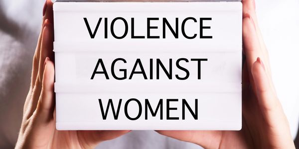 Lightbox sign reading 'Violence Against Women' held by hands.