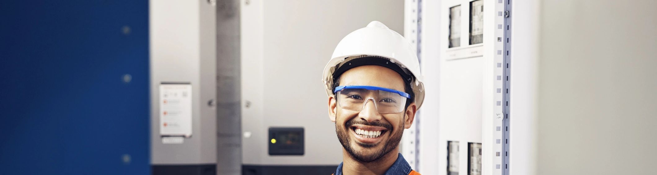Worker in hard hat and safety vest beside closed electrical cabinets