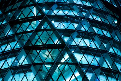 Close-up of a building's geometric glass facade illuminated in blue light.