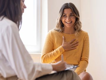 A woman in a yellow sweater expresses gratitude during a conversation.