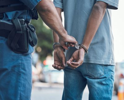 Police officer handcuffing a man standing outdoors.