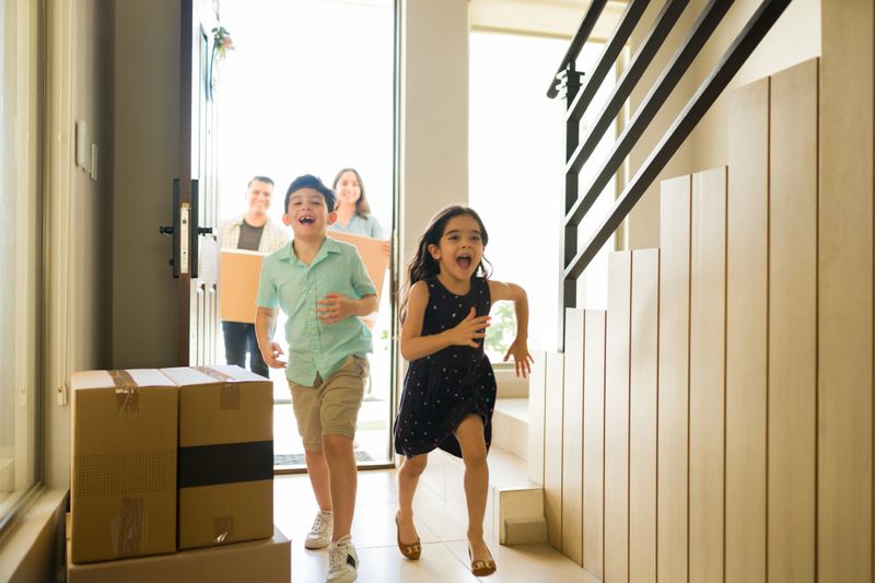 Very happy children running looking excited about moving in into a new house with mom and dad carrying boxes