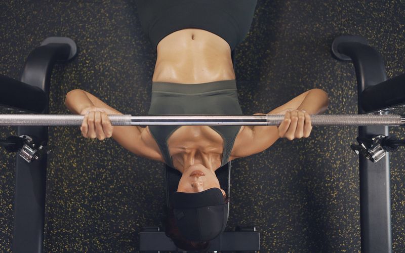 Sporty woman working out with barbell on bench in the gym.