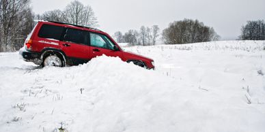 Red Subaru stuck in deep snow on a wintery road.