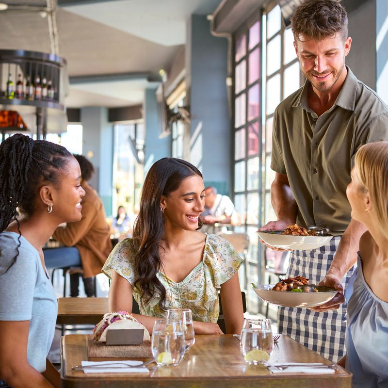 Group Of Female Friends Meeting Up In Restaurant Being Served Meal By Waiter