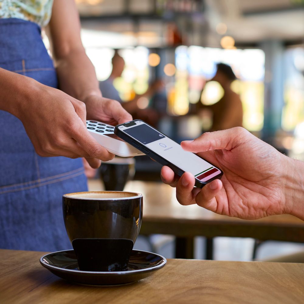 Customer paying for coffee using a mobile phone and contactless card reader.
