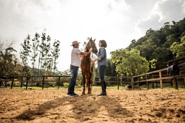 Two people with a horse in an outdoor paddock.