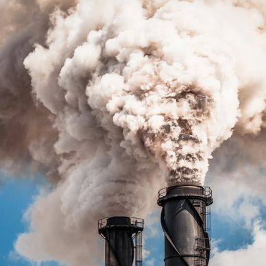 Thick smoke billows from two industrial chimneys against a blue sky.