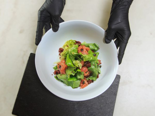 Hands in black gloves holding a bowl of fresh salad with greens and tomatoes.