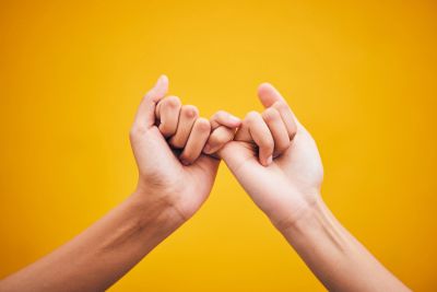 Two hands making a pinky promise against a yellow background.