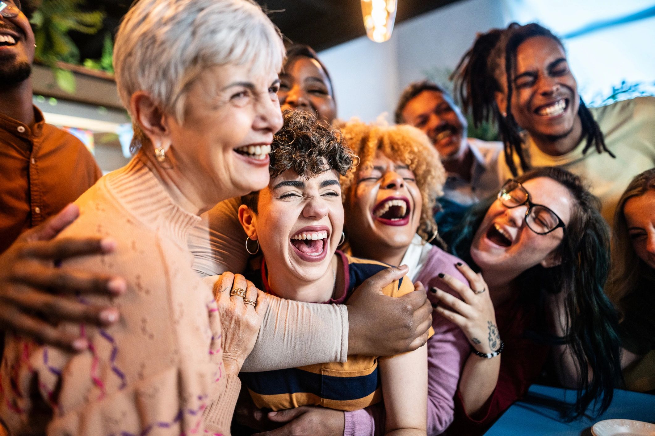 Group of diverse friends laughing and hugging joyfully indoors.