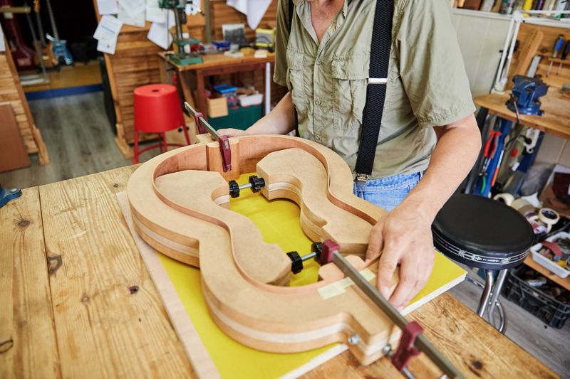 Unrecognisable man building a handcrafted guitar in his luthier's workshop.