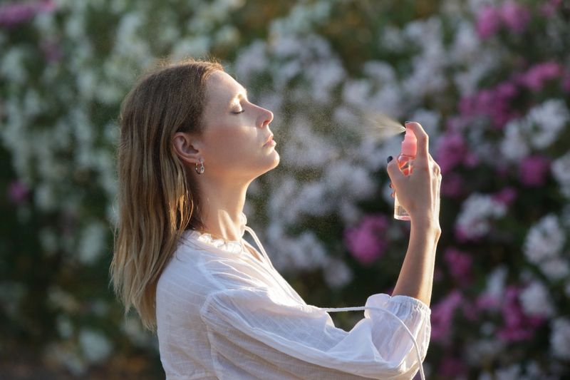 Woman spraying facial mist on her face, summertime skincare concept