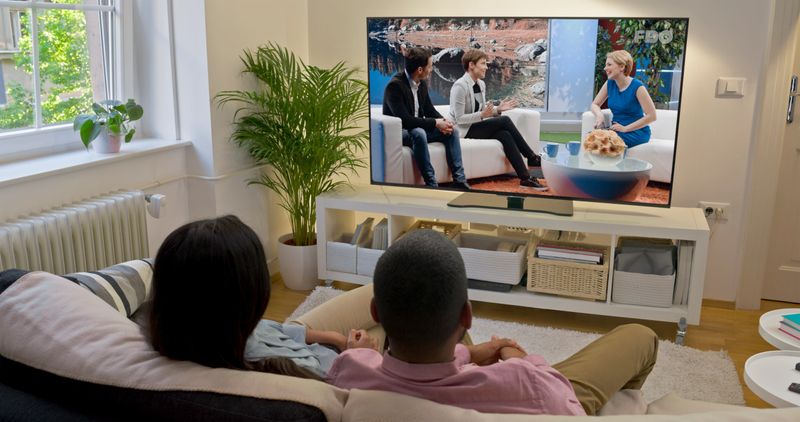 Rear view of couple watching television show while sitting on sofa in living room.