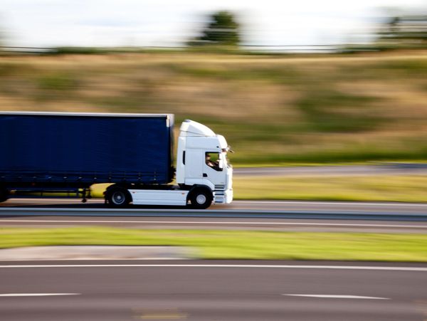 White truck with blue trailer moving fast on a highway.