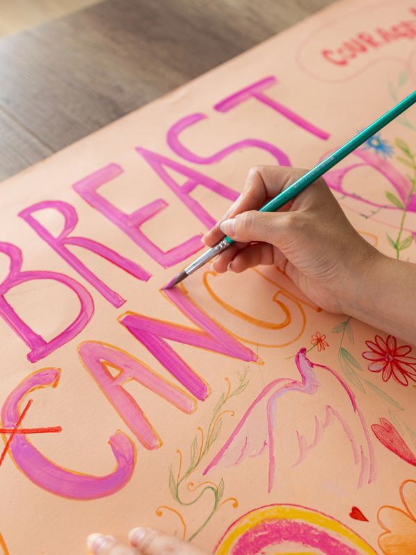 Hand painting colorful words and drawings on a poster.