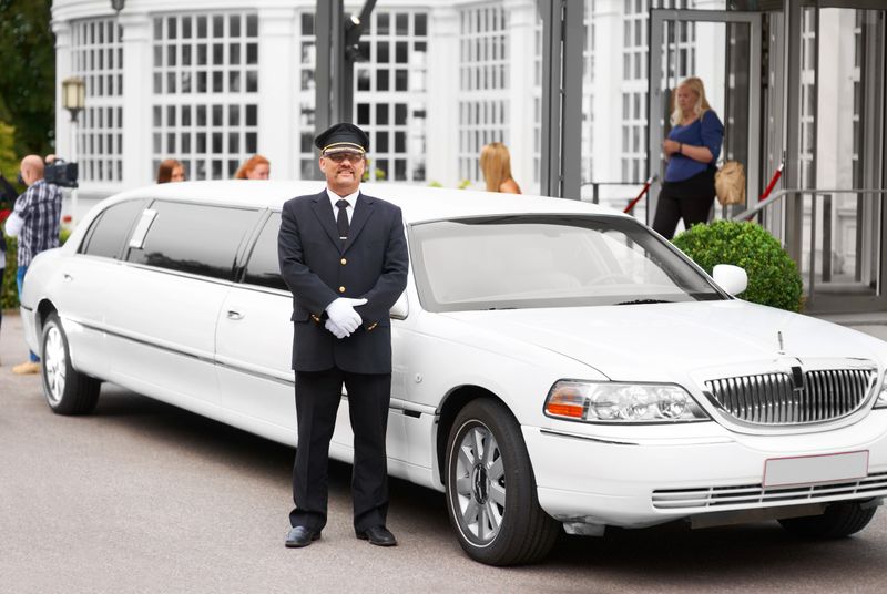A proud chauffeur standing beside a white stretch limousine
