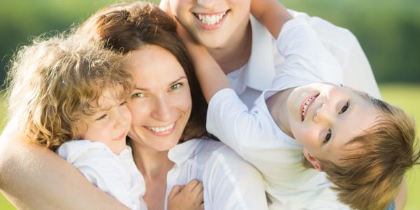 Happy family of four smiling and hugging outdoors on a sunny day.
