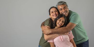 Happy family of three sharing a warm group hug and smiles.