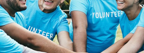 Group of volunteers joining hands in teamwork gesture outdoors.