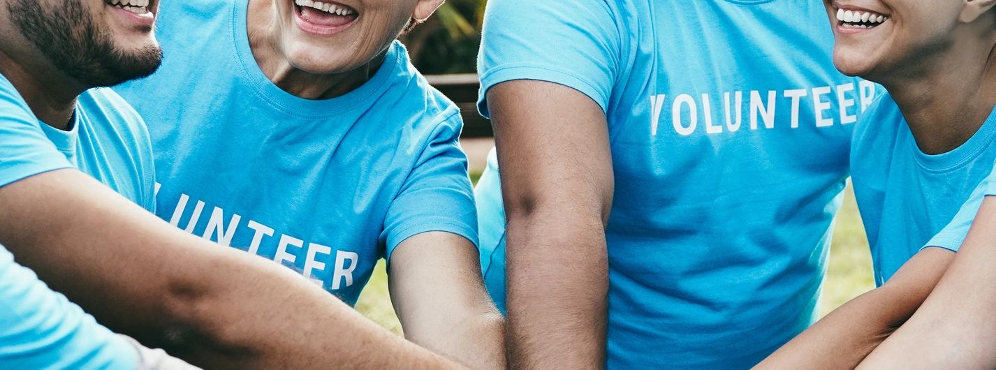 Smiling volunteers in blue shirts join hands in unity.