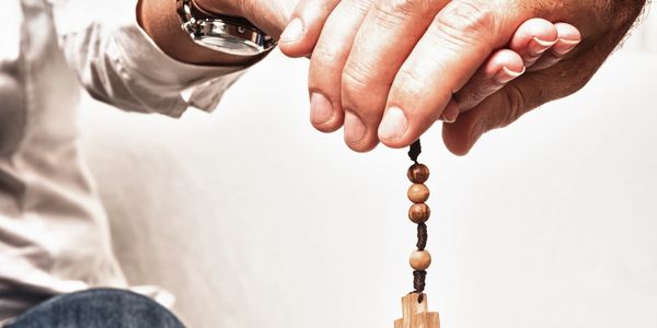 Two people holding hands with a wooden cross rosary bead.