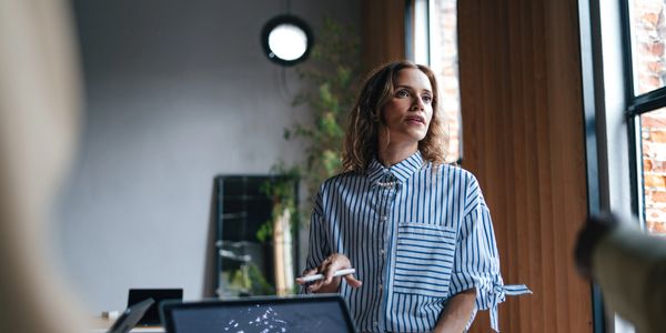 Woman in striped shirt looking thoughtfully out a window in a modern office.