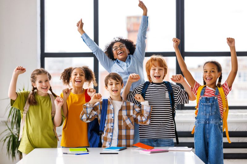 Group of schoolchildren and teacher standing together, celebrate   successful completion of collective school work and   raising their hand in class during lesson