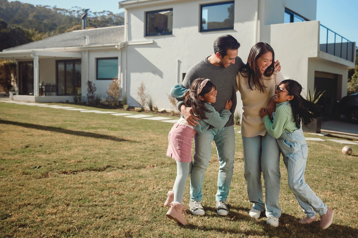 Happy family hugging and laughing outside their home on a sunny day.