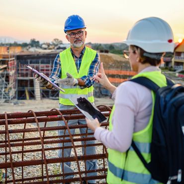Two construction workers discussing project details at a site during sunset.