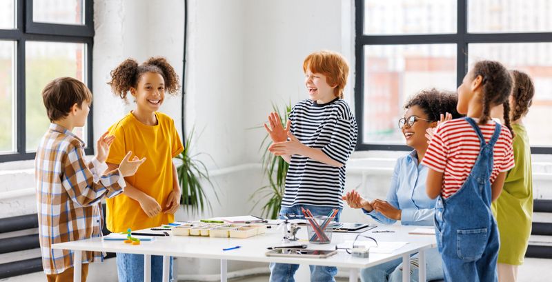 Happy teacher and joyful school kids celebrate together  successful completion of collective school work in a light classroom