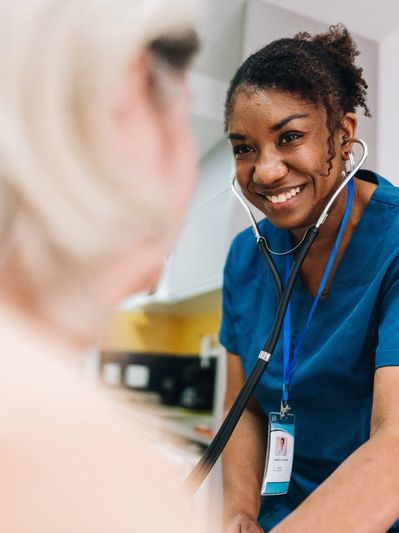 Smiling nurse using a stethoscope to check a patient's heartbeat.