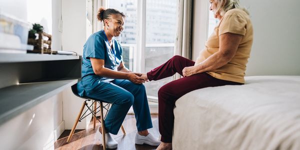 Nurse checking elderly woman's foot in a bright room.