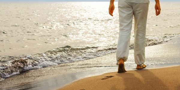 Person walking barefoot on a sandy beach by the ocean shore.