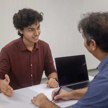 Two men engaged in a discussion with a laptop on the table.