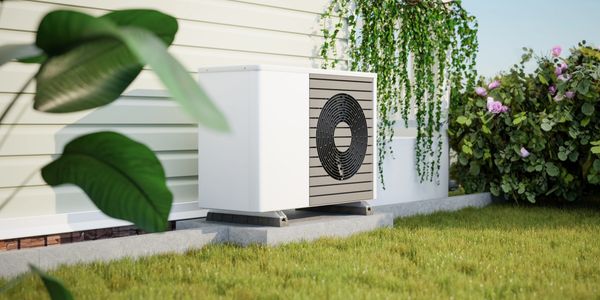 Outdoor air conditioning unit beside a house with plants and grass.