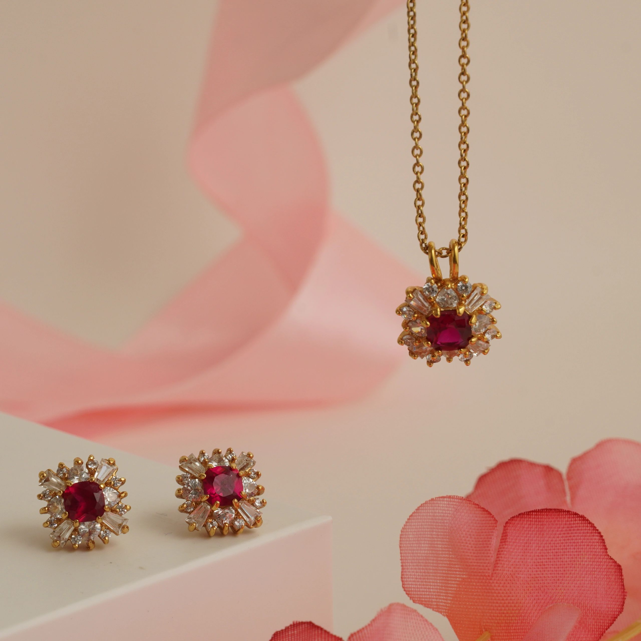 Gold jewelry set with ruby and diamond accents on a soft pink background.