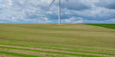 Wind turbine standing in a striped green and brown field under a cloudy sky.