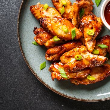 Glazed chicken wings garnished with green onions and served with a side of dipping sauce.