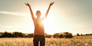 Person with arms raised in a sunlit field.
