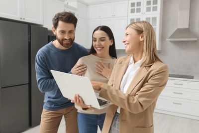 Three people in a kitchen looking at a laptop.