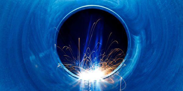 Bright sparks inside a blue metal pipe during welding.